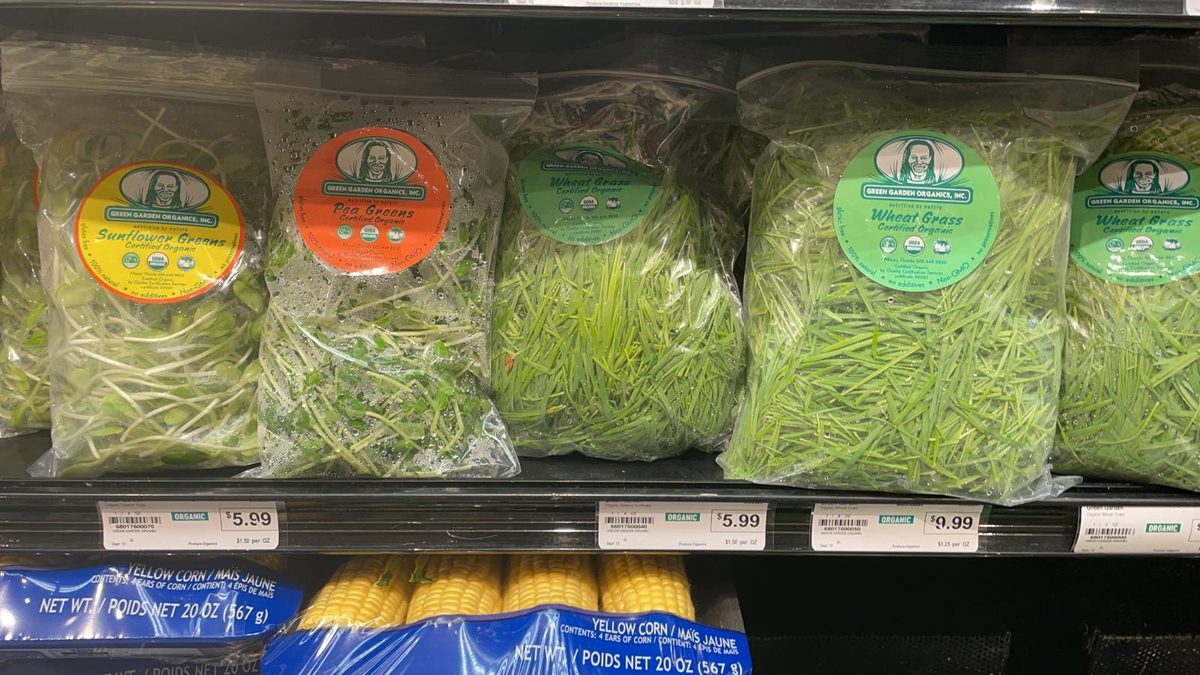Store refrigerator shelf holding bagged Green Garden Organics sunflower greens, pea greens and wheatgrass with price labels
