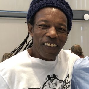 Lou Duncanson of Green Garden Organics smiling, wearing a dark knit cap and a white T-shirt